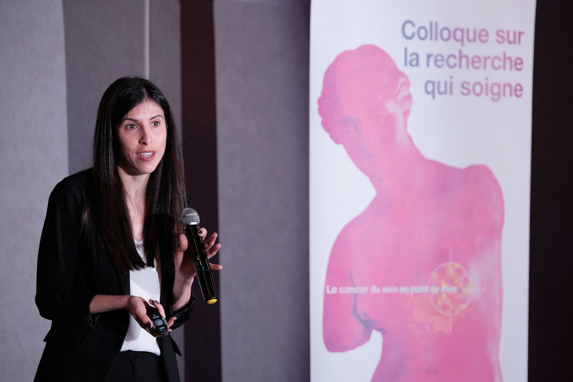 Une conférencière prend la parole devant l'affiche du Colloque sur la recherche qui soigne